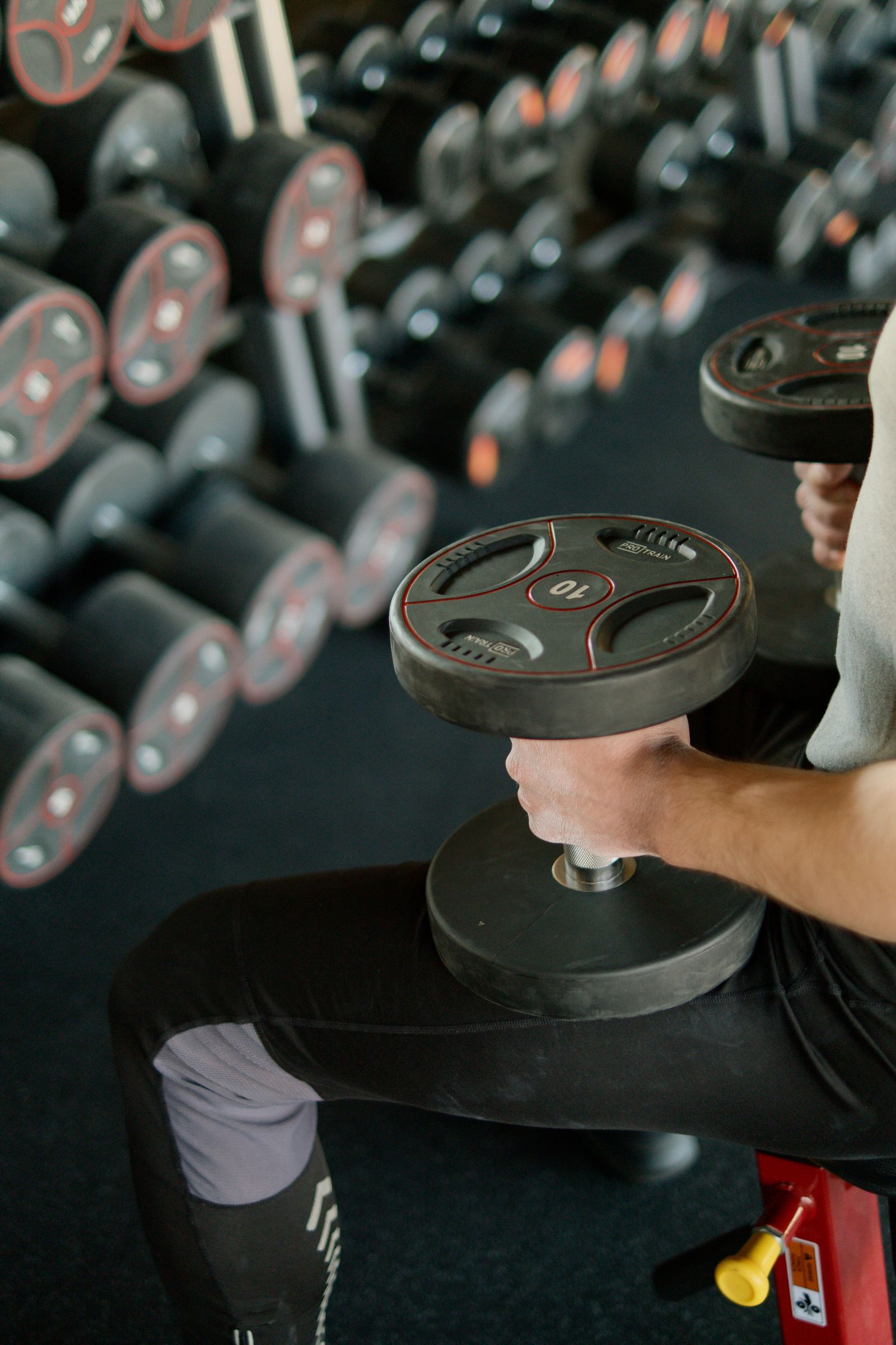 Person seated on a bench holding a dumbbell beside a dumbbell rack